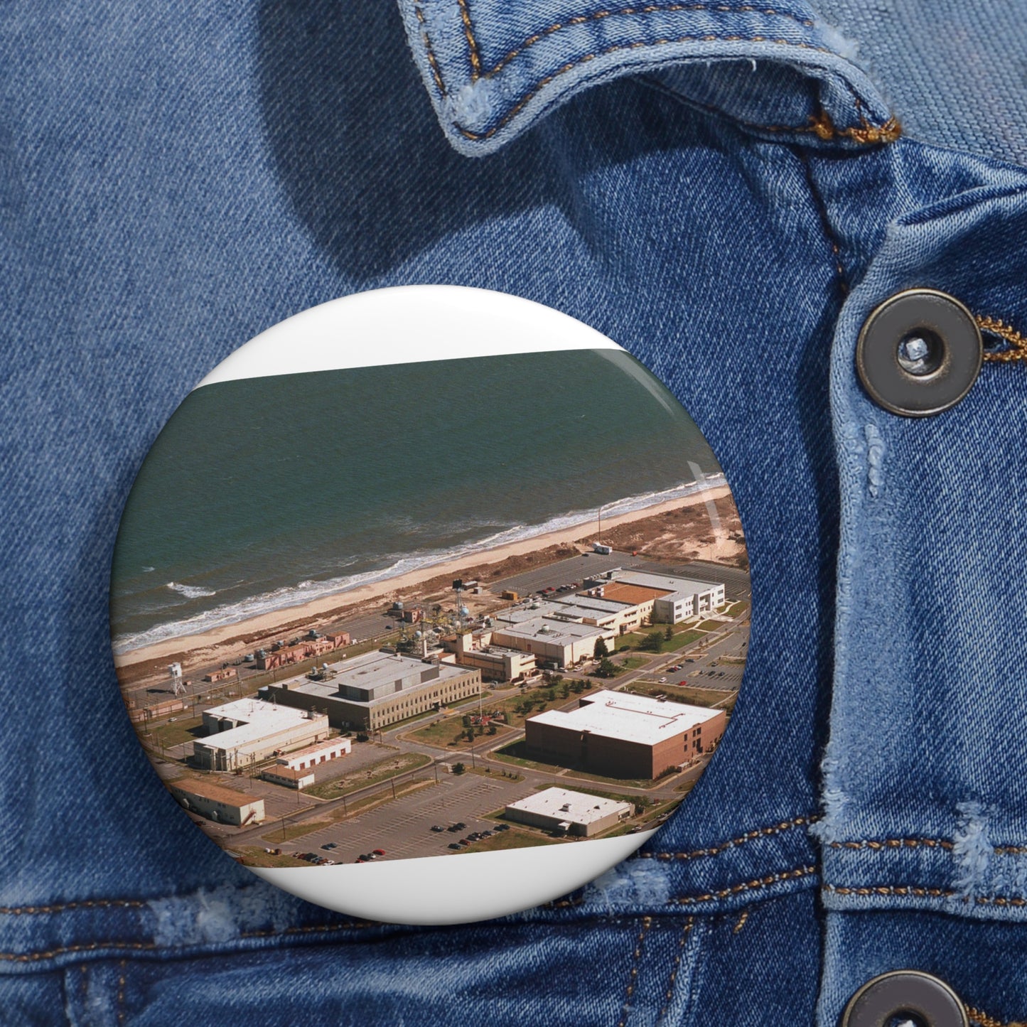 An aerial view of the Naval Surface Warfare Center testing building on the Dam Neck Naval Base. Along the beach are various types of gun mounts with their associated fire control radars atop the test building Pin Buttons with Crisp Design